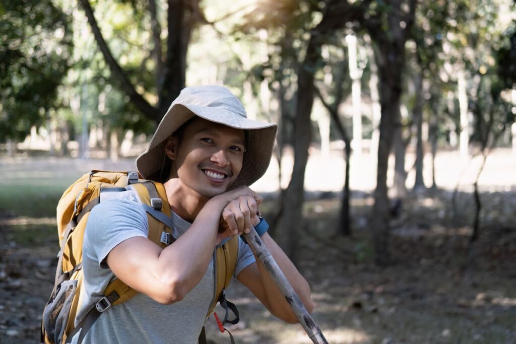 Imagem mostra jovem feliz fazendo trilha com chapéu, um dos itens para levar em um passeio de cachoeira.