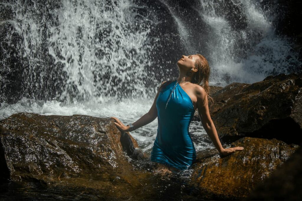 Imagem mostra jovem se refrescando em cachoeira.